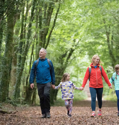 a family enjoying a leisurely walk together along a lush, tree-lined path in a woodland park, in County Clare