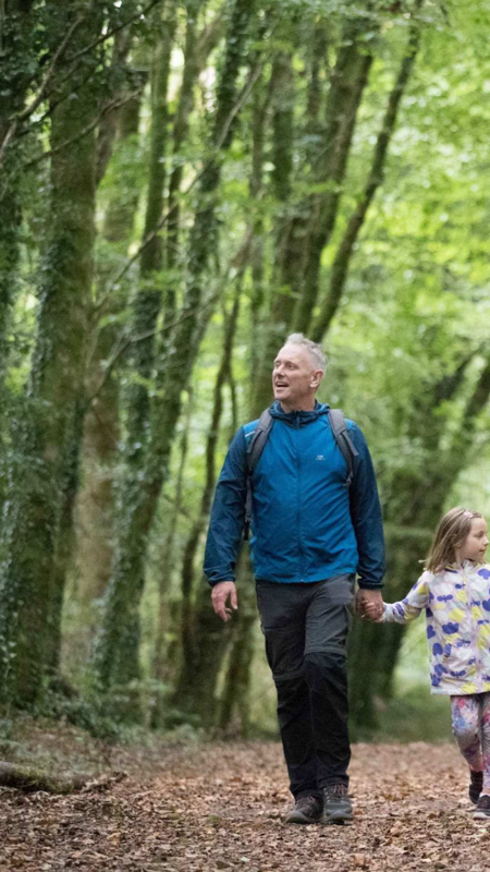 a family enjoying a leisurely walk together along a lush, tree-lined path in a woodland park, in County Clare