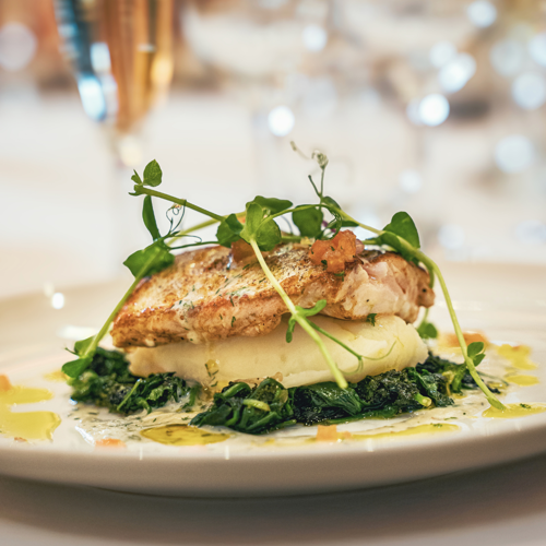  a pan-seared fish fillet (resembling halibut or whitefish) resting on a layer of mashed potatoes and dark greens 